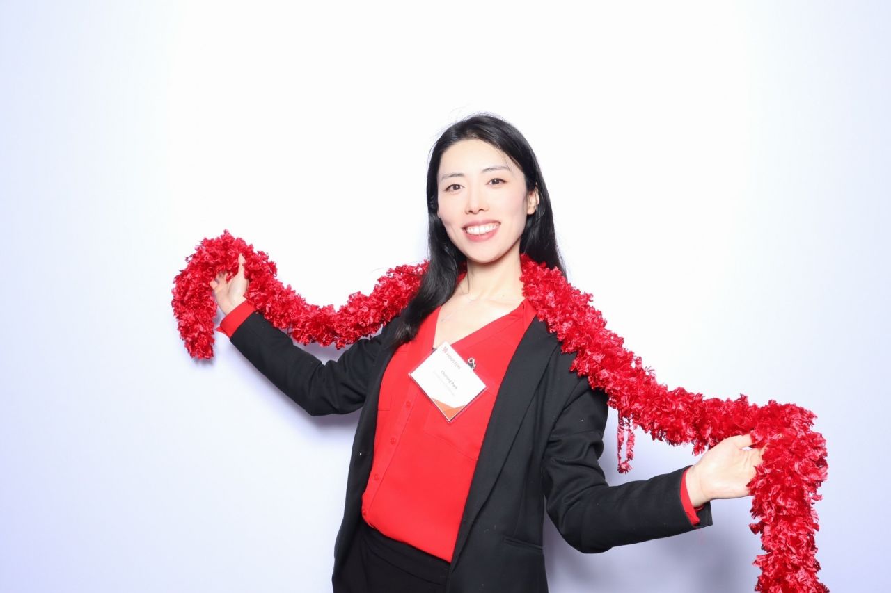 Portrait from the faculty announcement, with red attire and a red garland against a light background.