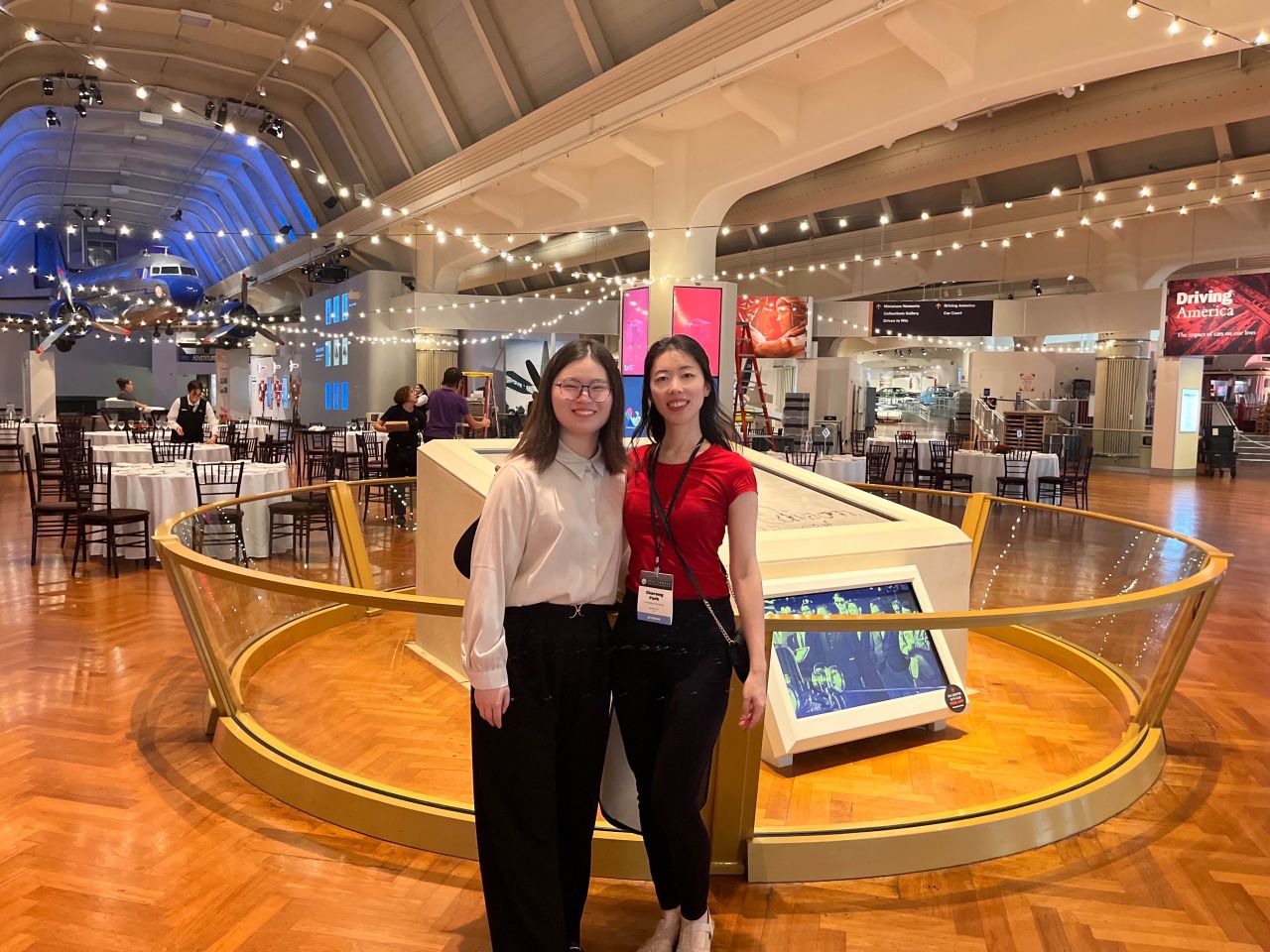 Two attendees pose beside a display in a museum-style event space.