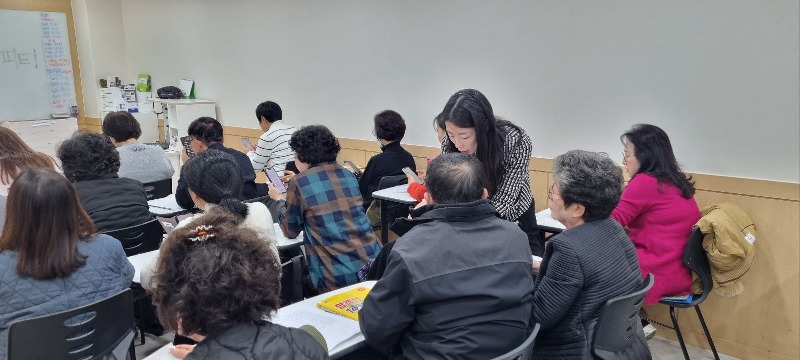 An instructor leans over to help a participant during a classroom exercise.