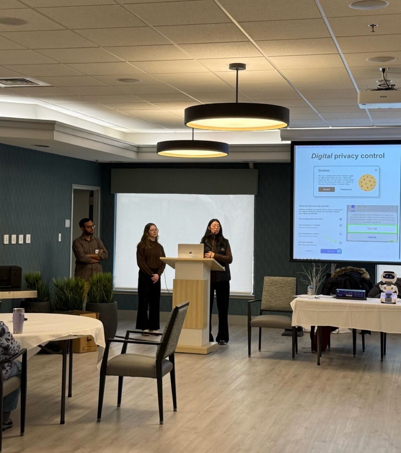 Three presenters stand at the front of a room beside a digital privacy slide.