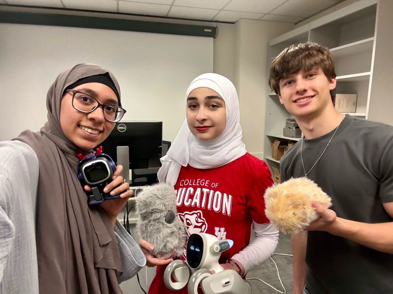 Three lab participants pose with several small companion robots.