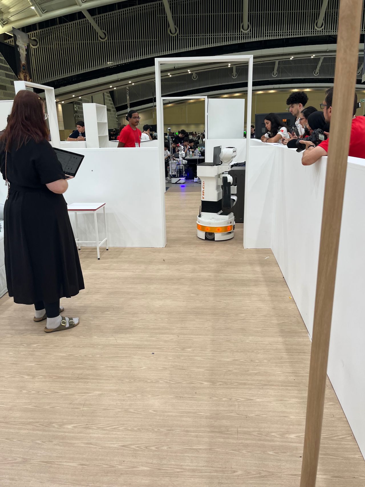 Visitors watch a robot demonstration inside a partitioned indoor arena.