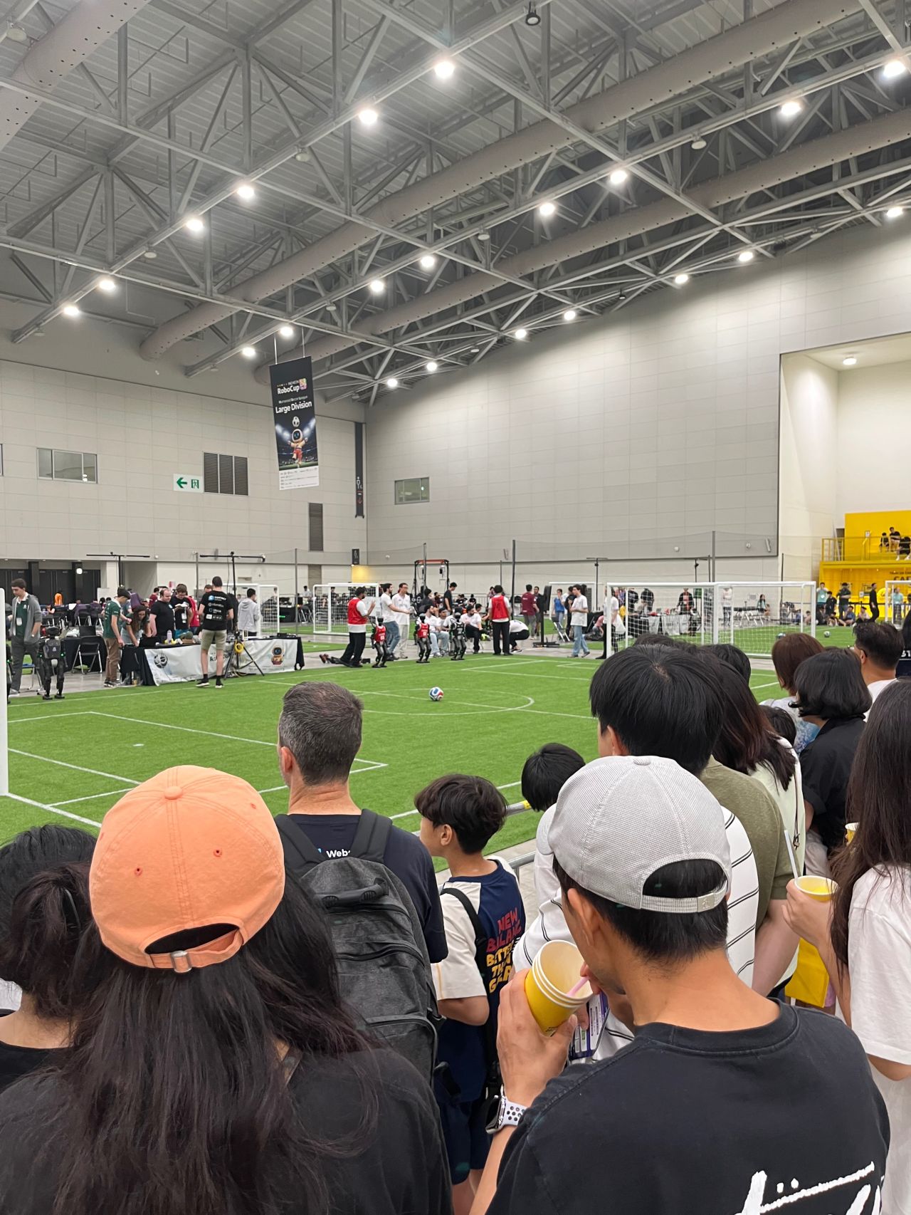 Spectators watch activity on an indoor robot soccer field.