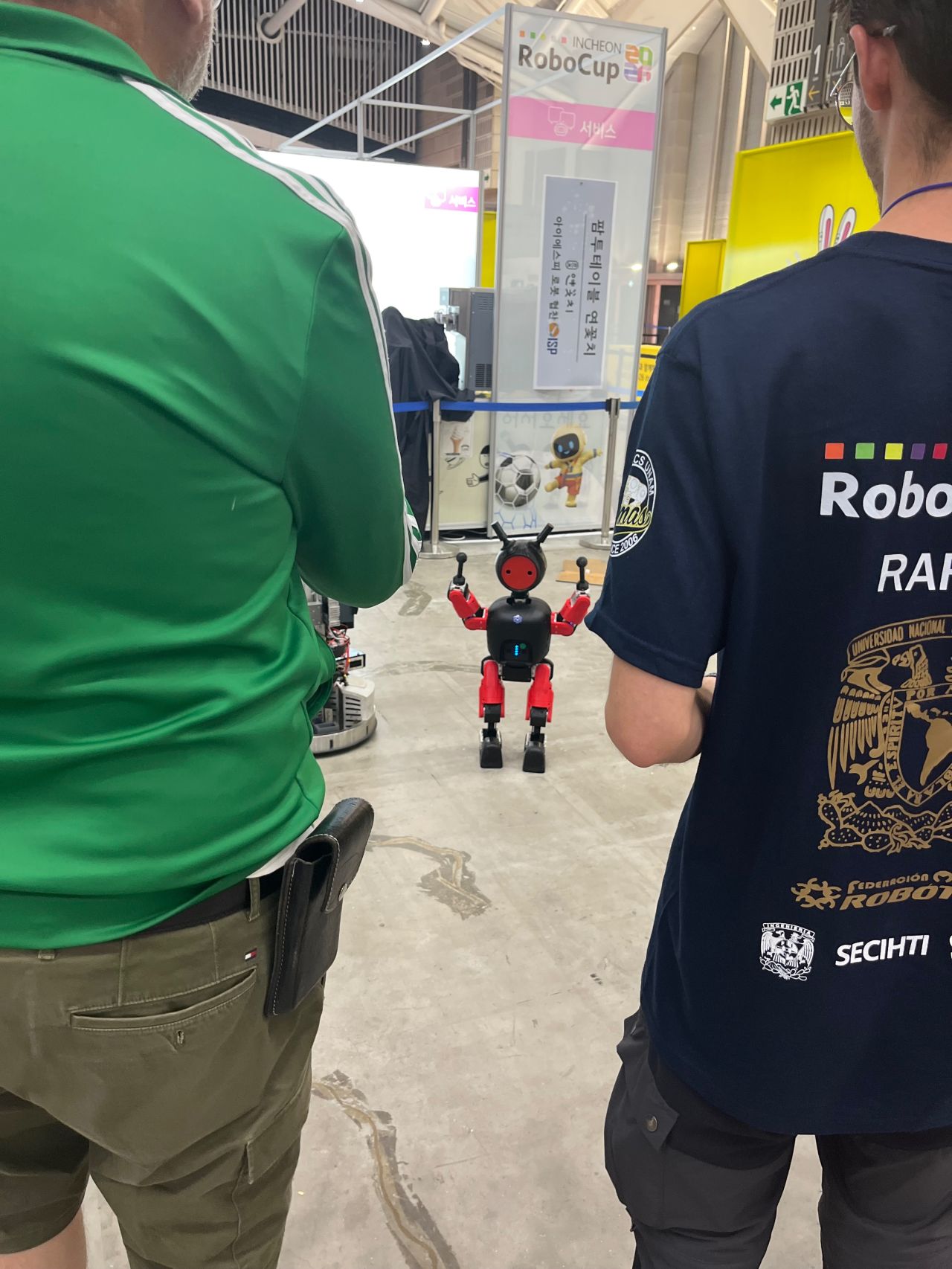 A small red-and-black humanoid robot stands between spectators.