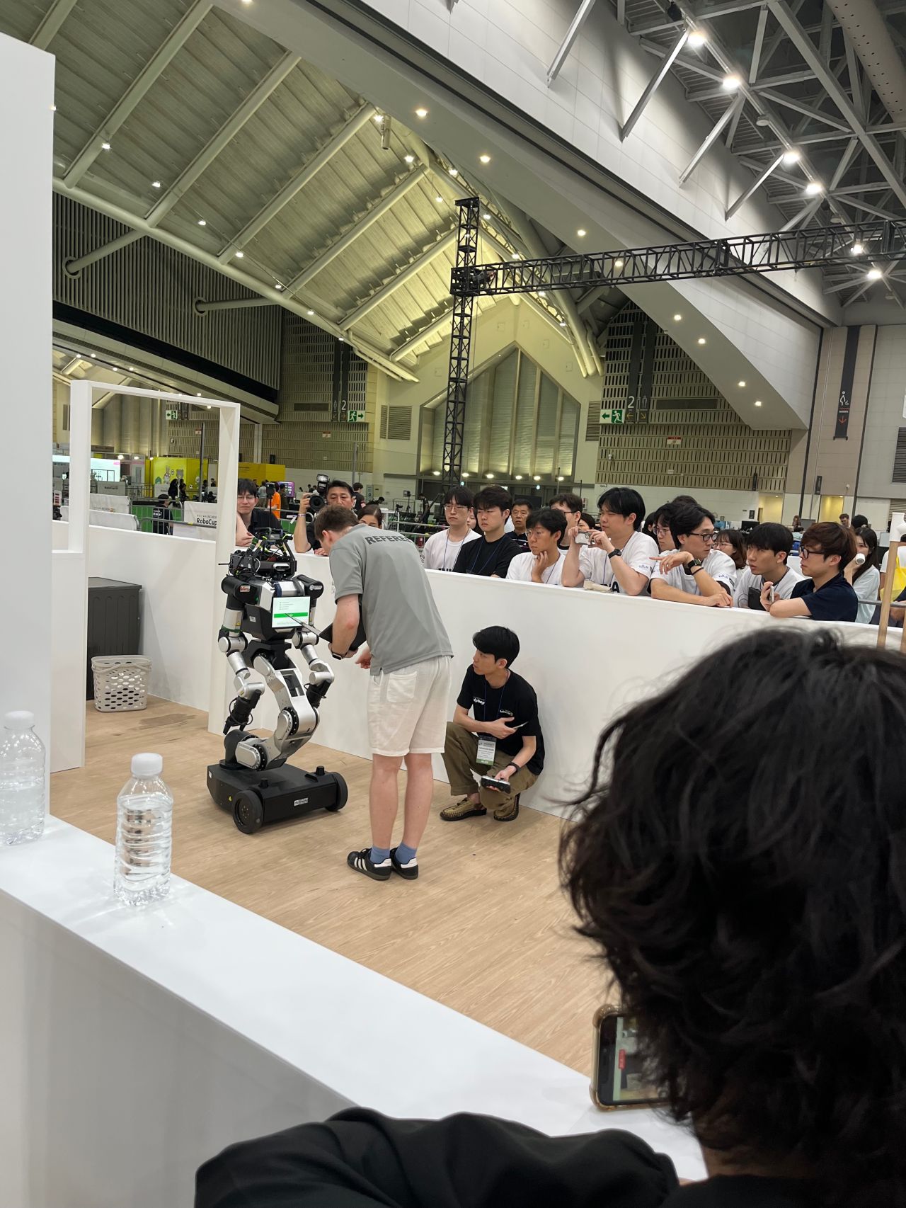 Participants crouch beside mobile robots in an indoor demonstration area.