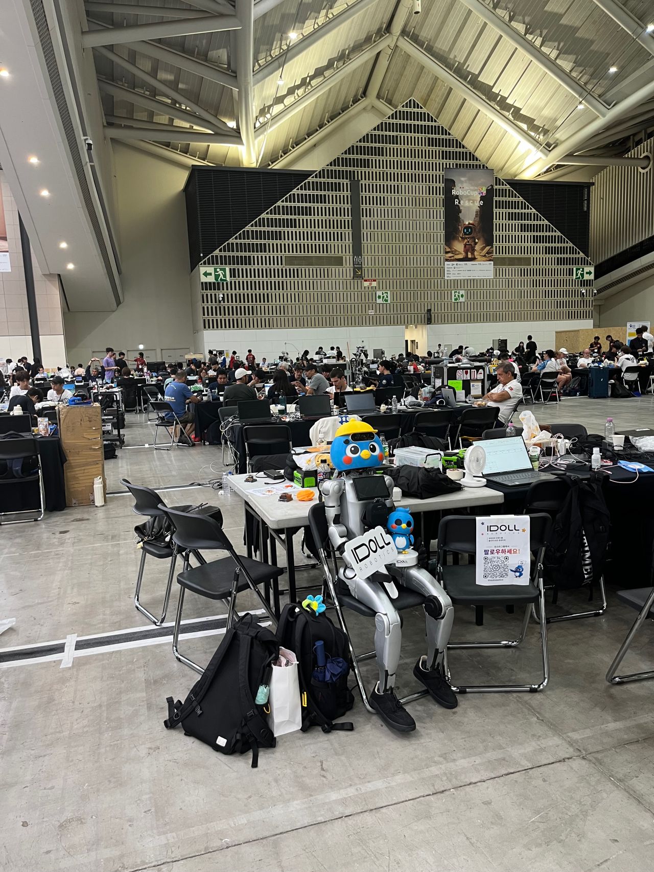 Service robots stand among worktables inside a busy exhibition hall.