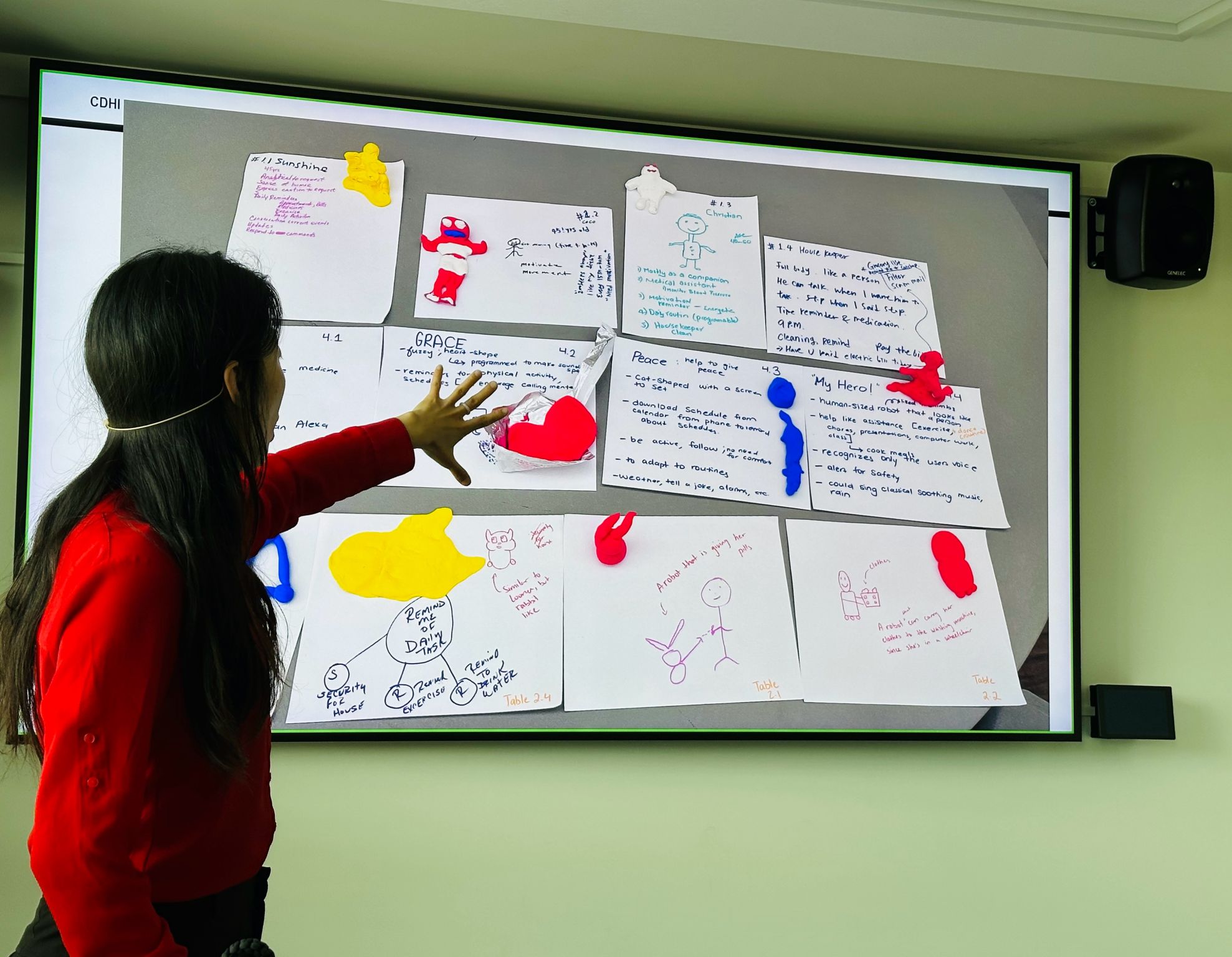 A presenter points to a slide containing participant drawings and handwritten worksheets.