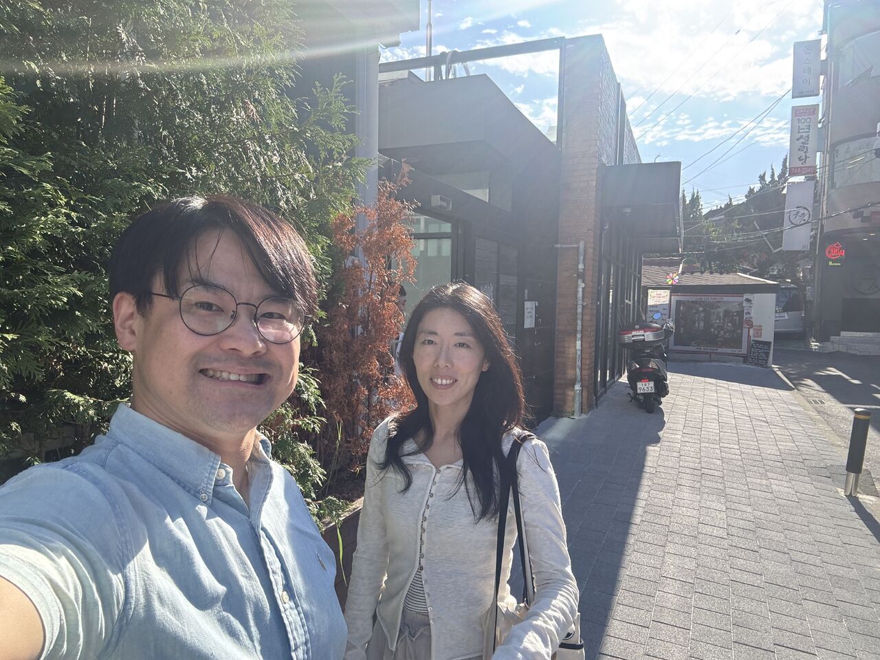 Two visitors pose together on a sunlit pedestrian path.