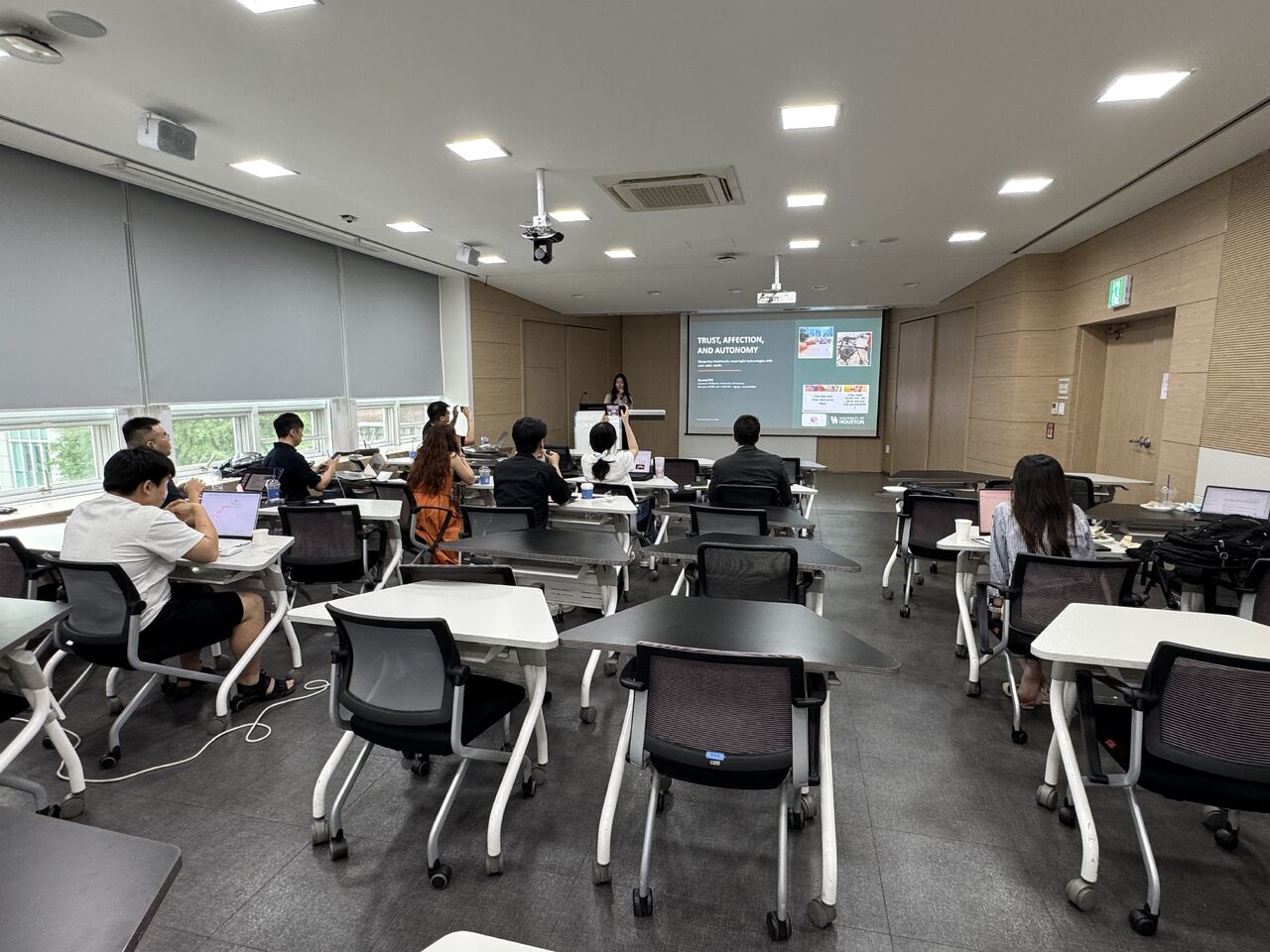 A classroom audience watches a projected research slide.