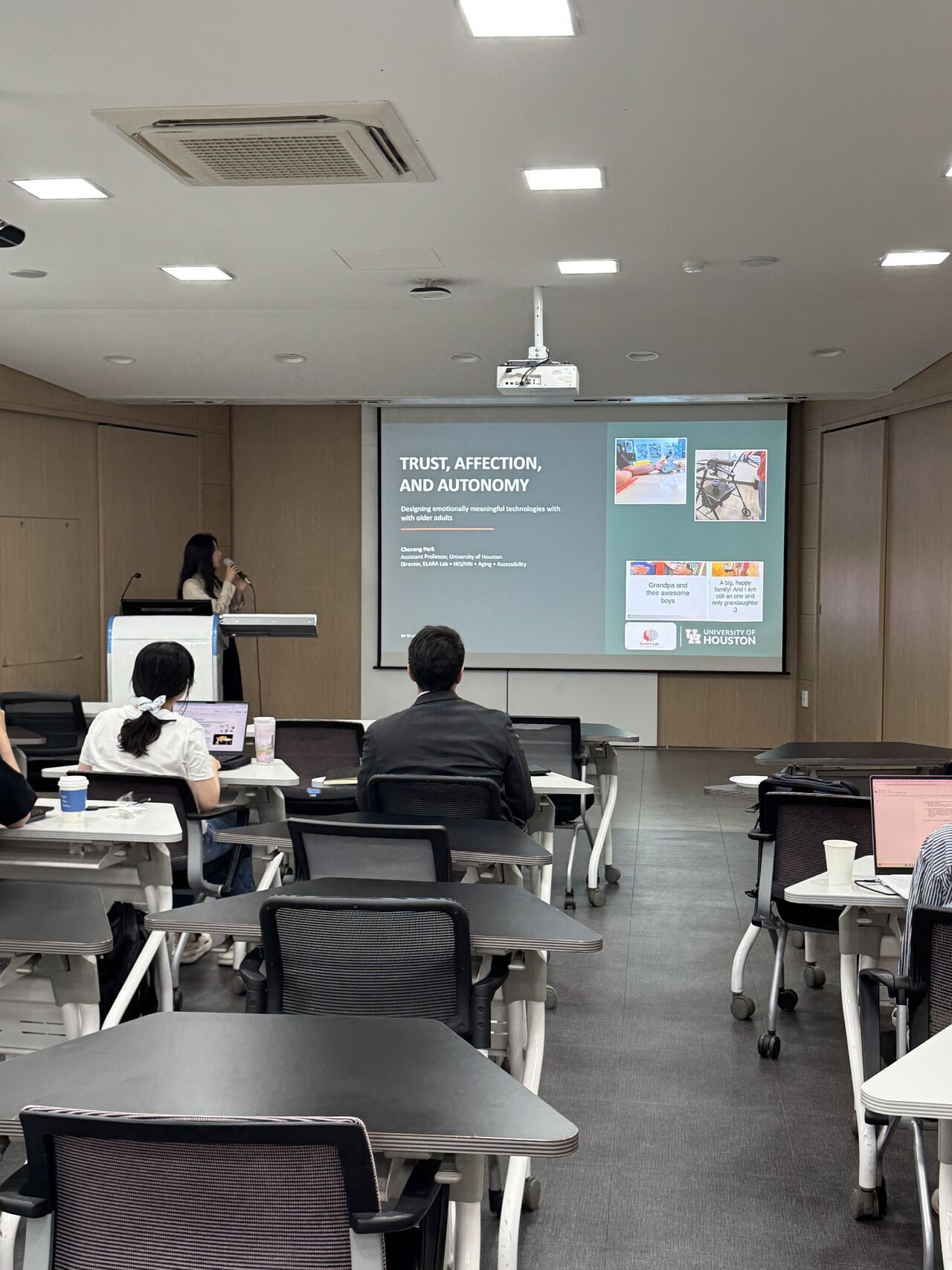 A presentation slide is shown at the front of a university classroom.