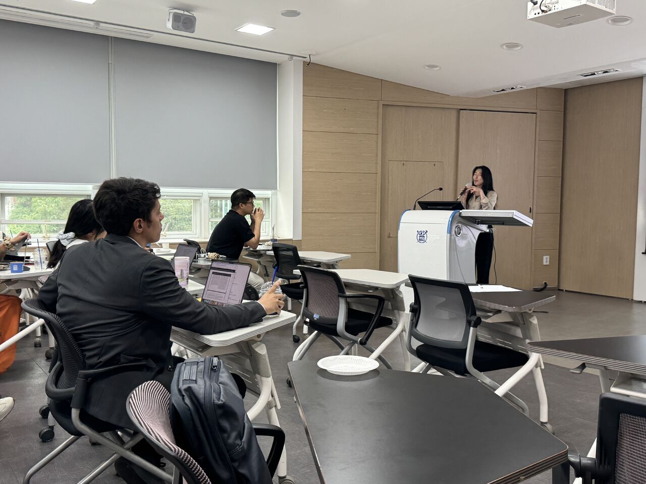 A classroom audience watches the presenter at the front of the room.