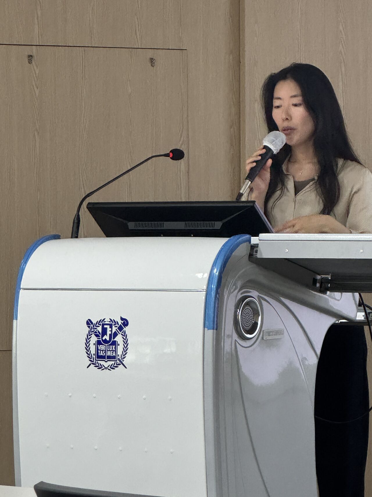 A presenter speaks behind a lectern with a university emblem.