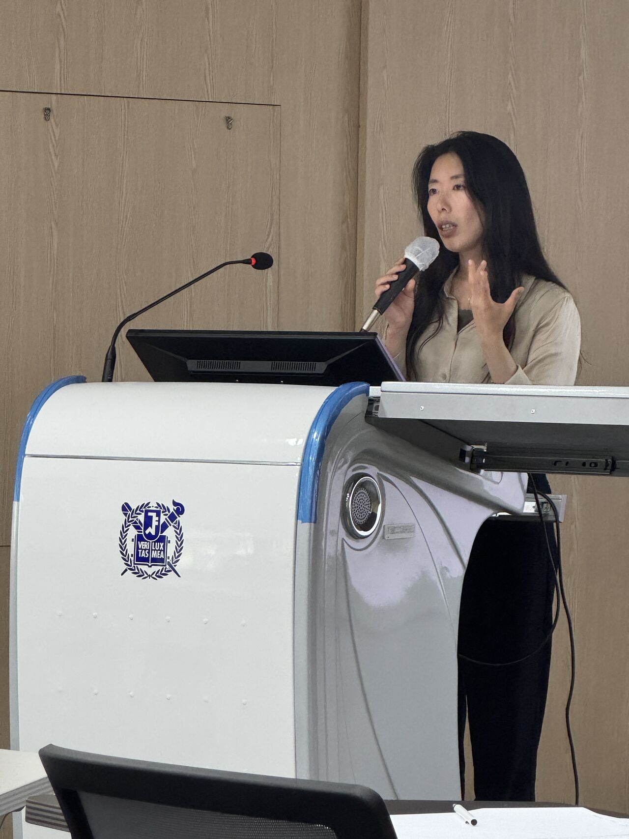 A presenter smiles while addressing the room from the lectern.