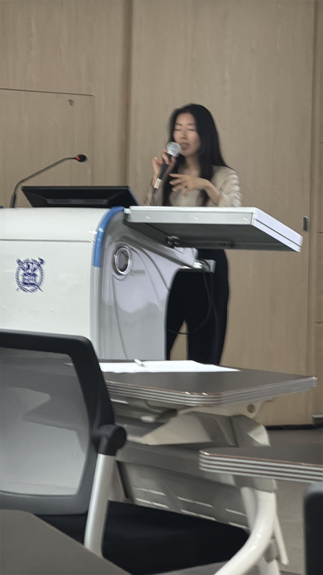 A presenter gestures while speaking beside a lectern.