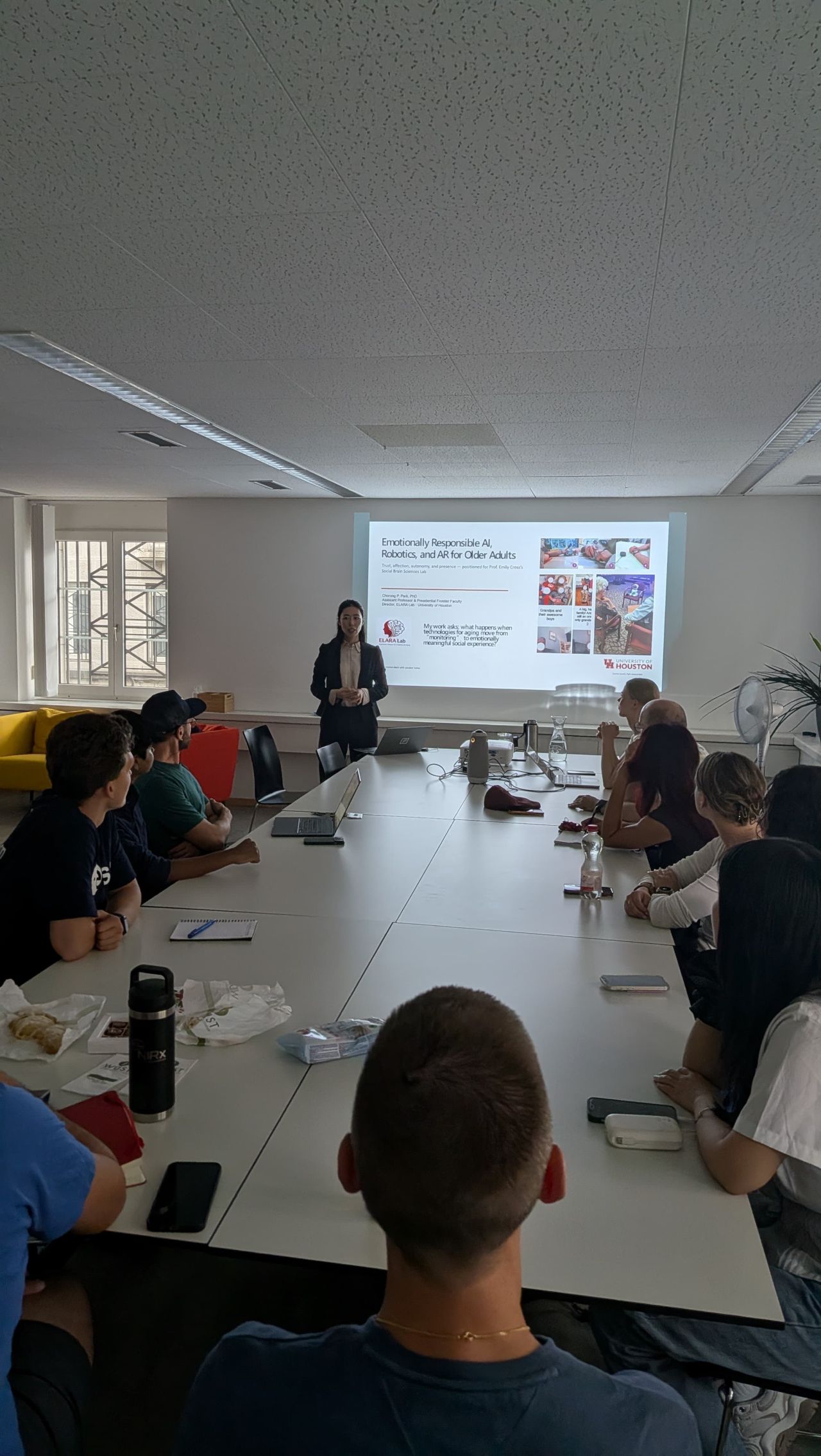 A research group sits around a long table facing a presentation screen.