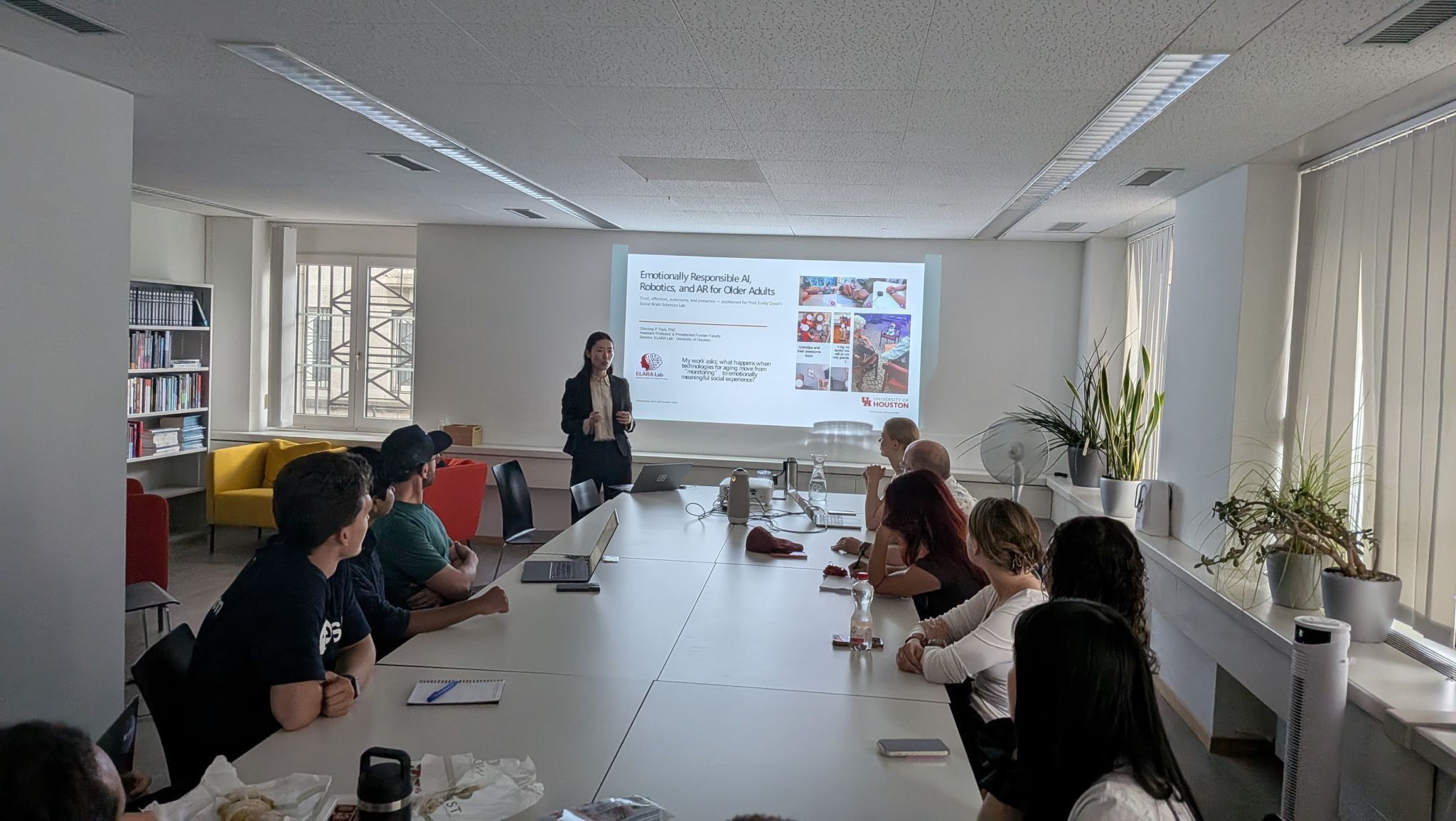 A presenter discusses a slide in a bright meeting room with bookshelves.