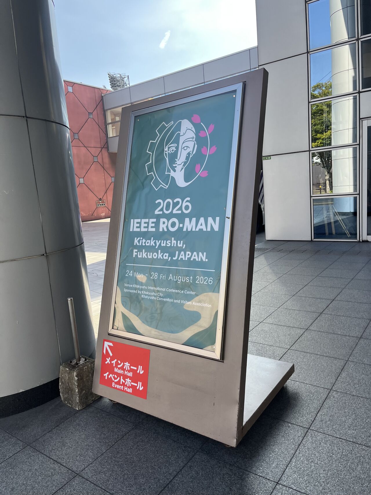 A freestanding sign welcomes attendees to IEEE RO-MAN 2026 in Kitakyushu.
