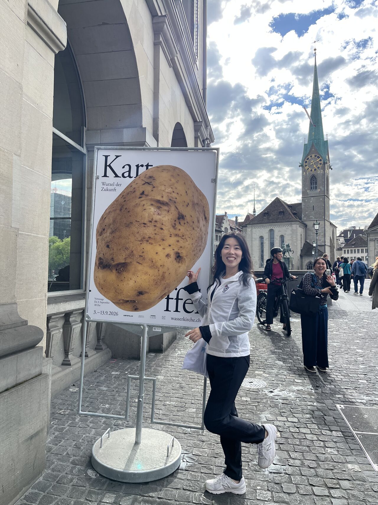 A visitor poses beside a shop sign on a city street.