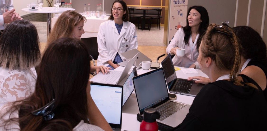 A small group discusses its work around a table with laptops.