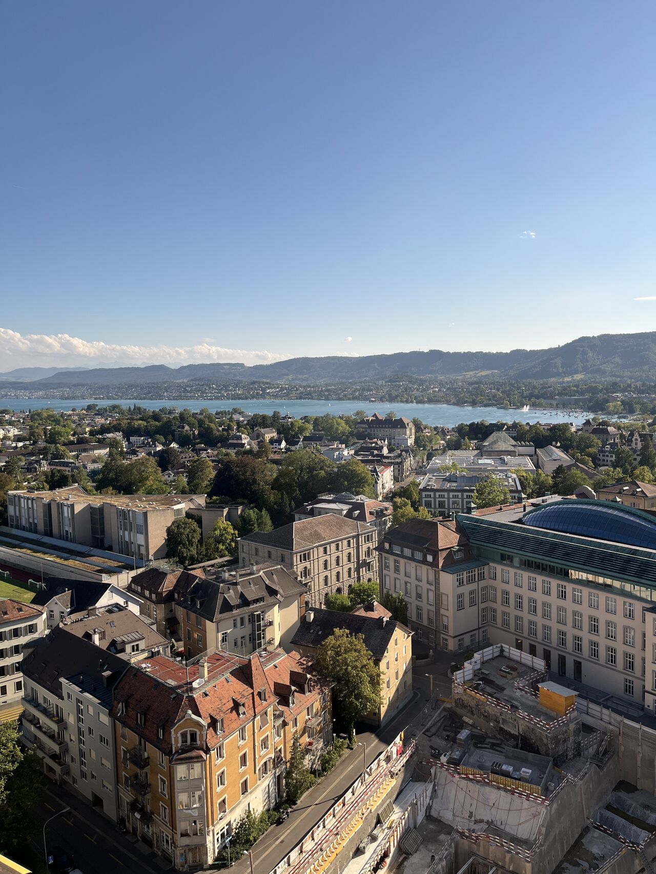 A high viewpoint shows city buildings, the lake, and distant hills.