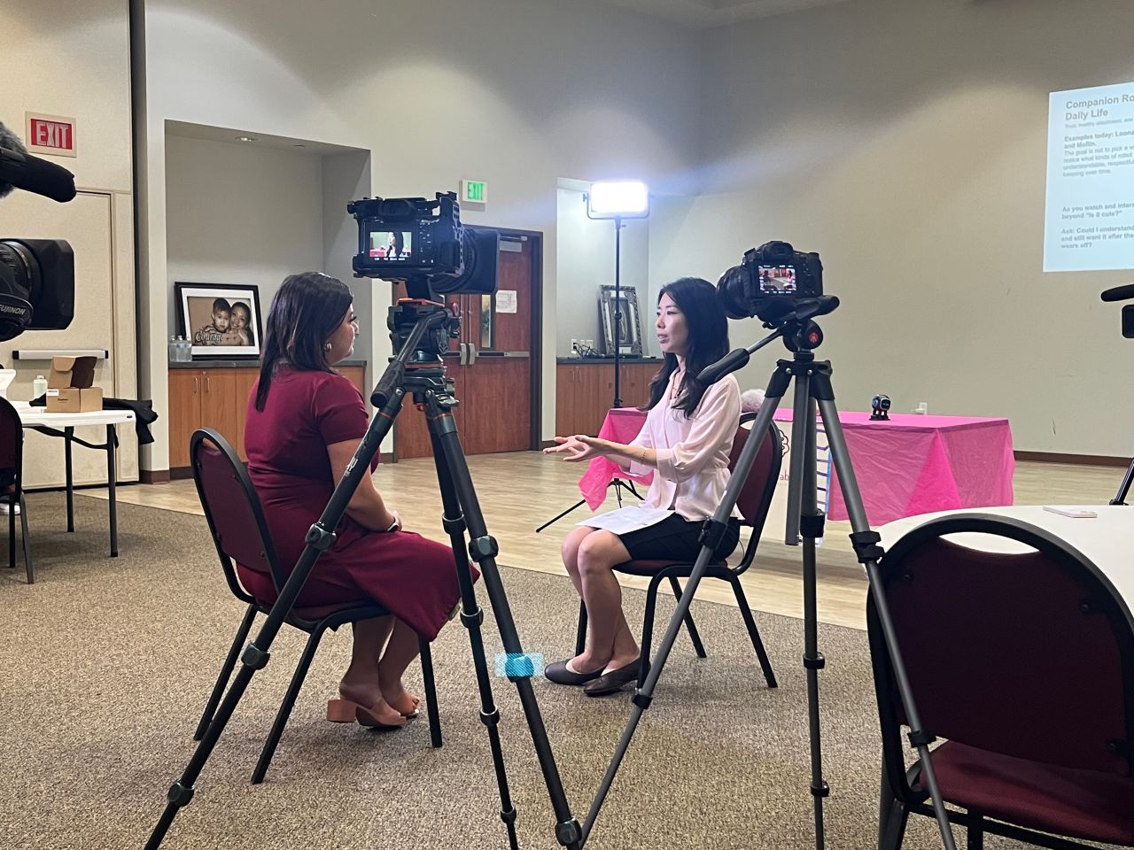 Two people sit facing each other during a filmed interview at a community center.