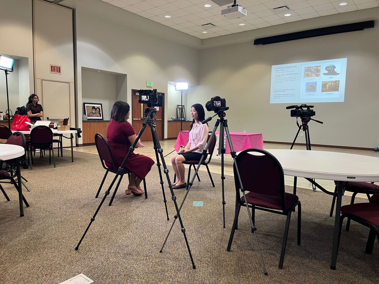A wide view of cameras, lights, and a seated community-center interview.