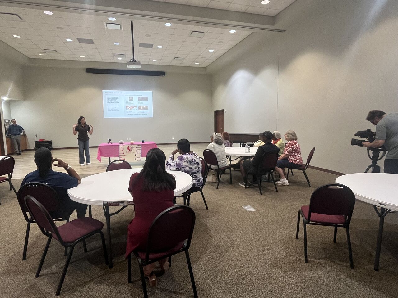 Community members sit around tables facing a presentation screen.