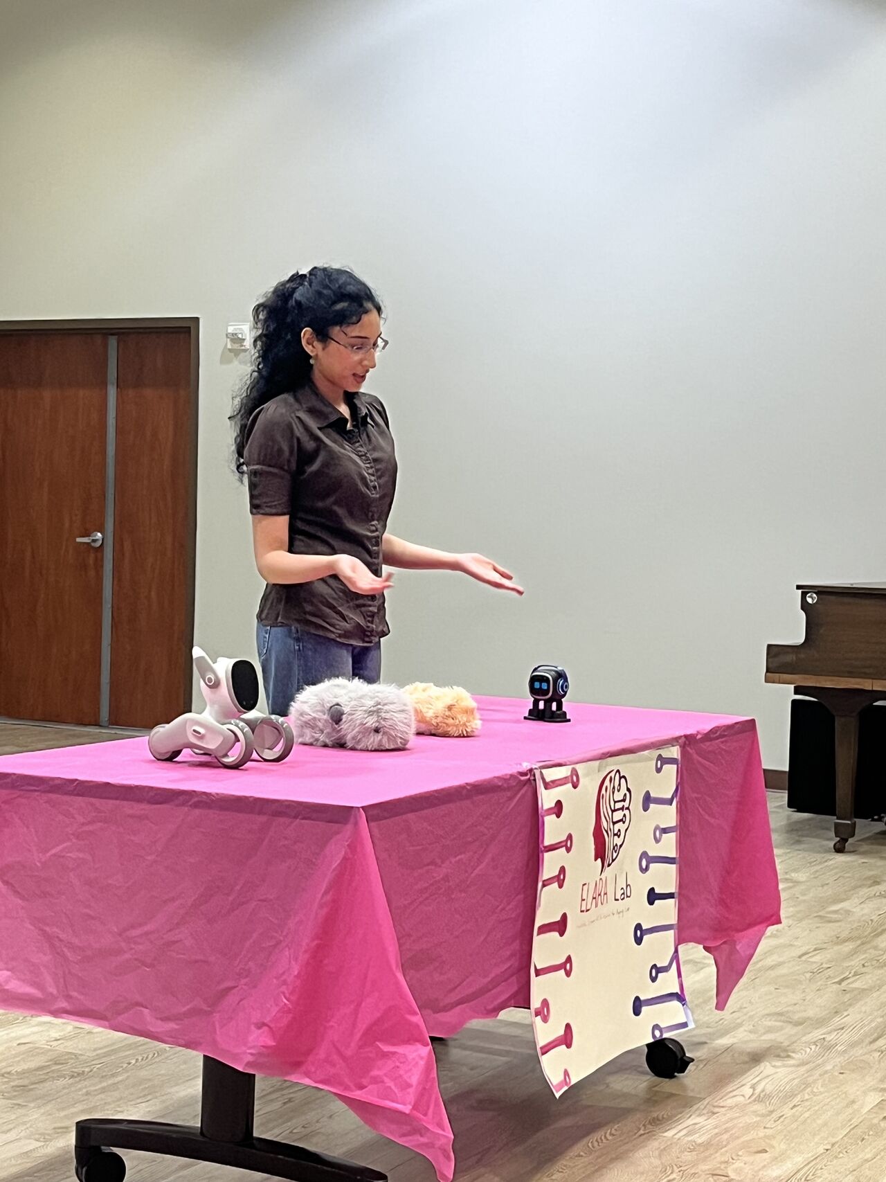 A presenter stands behind an ELARA Lab table displaying companion robots.