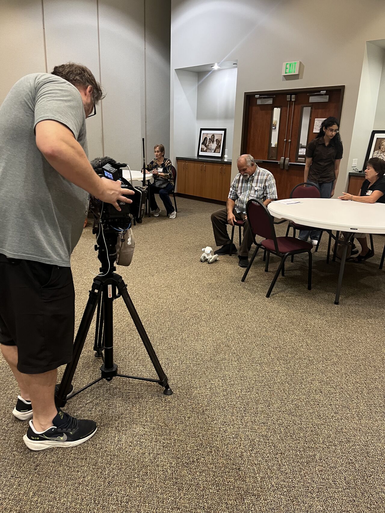 A camera operator films participants at a community-center table.
