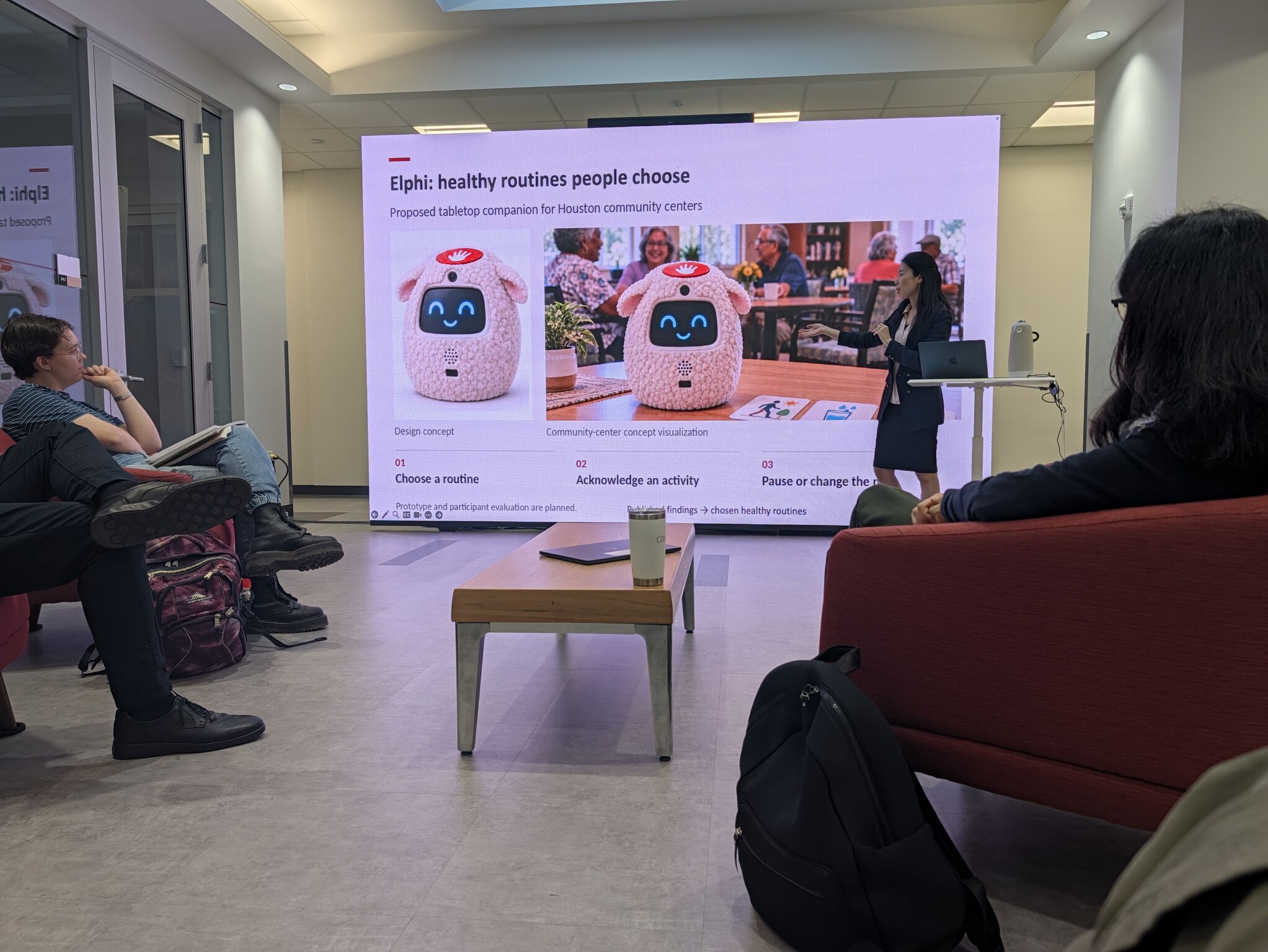 A presentation slide shows Elphi design concepts beside a speaker and seated attendees.