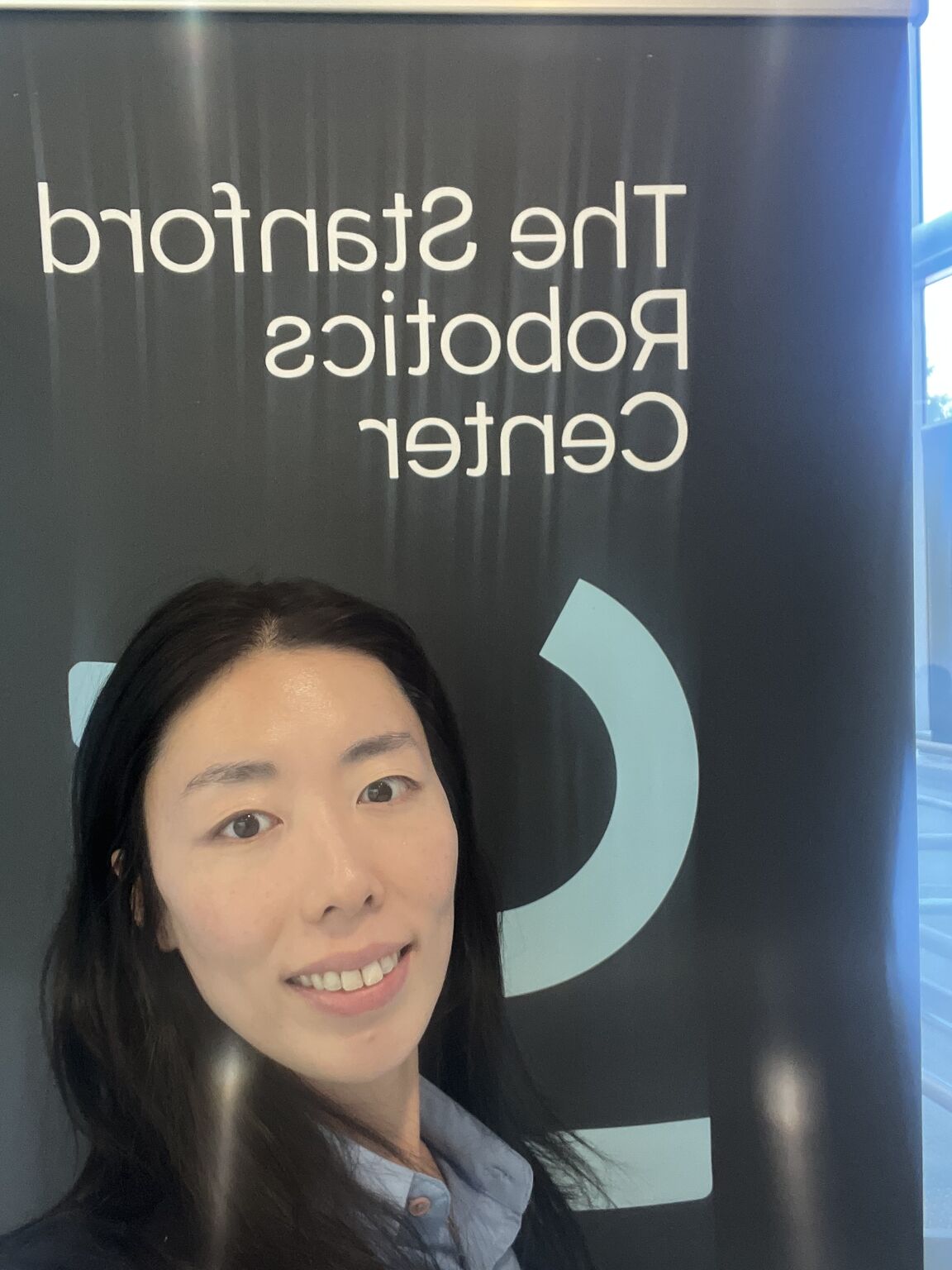 A visitor takes a selfie in front of a Stanford Robotics Center banner with mirrored lettering.