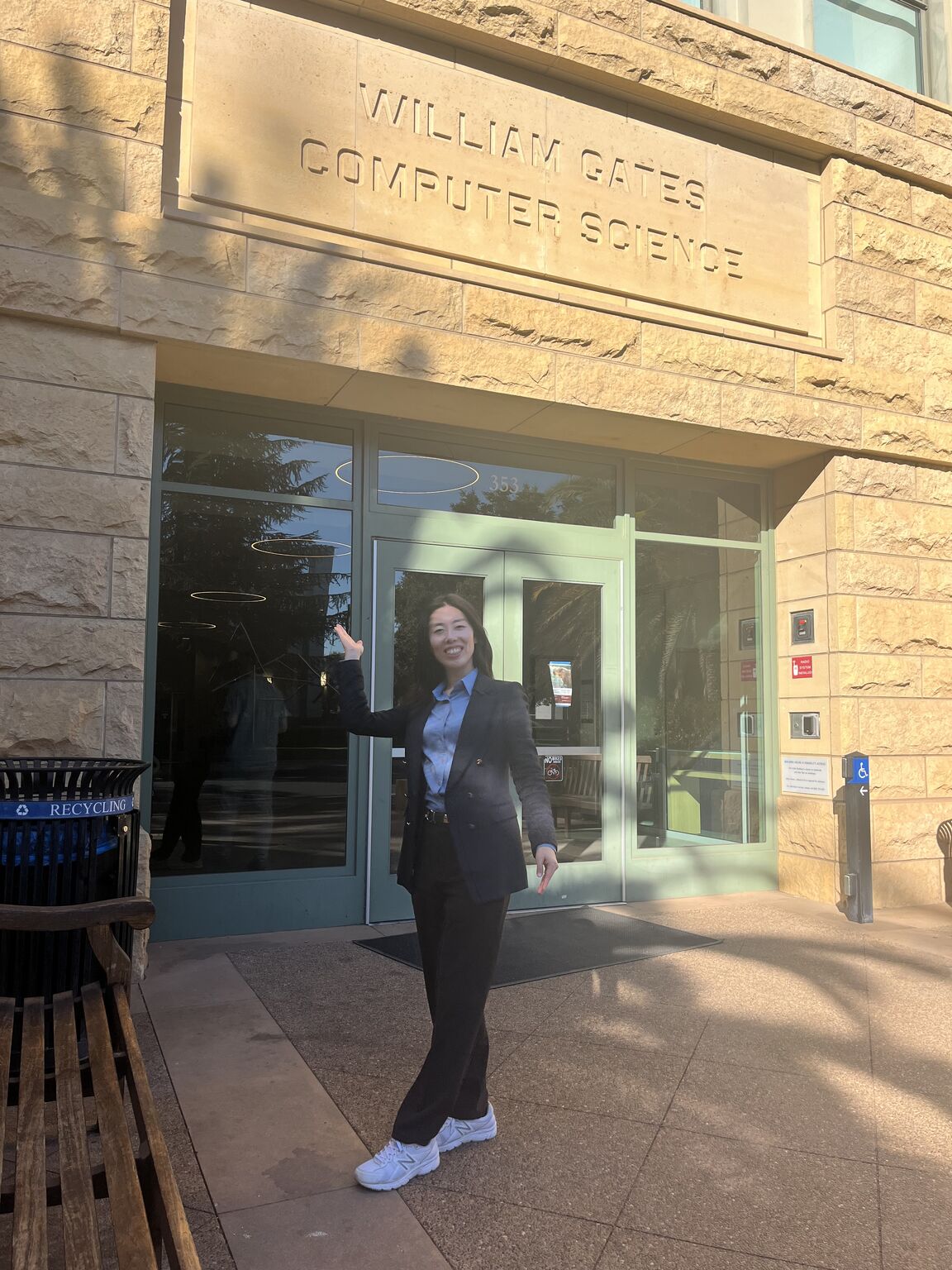 A visitor gestures toward the William Gates Computer Science sign above a building entrance.